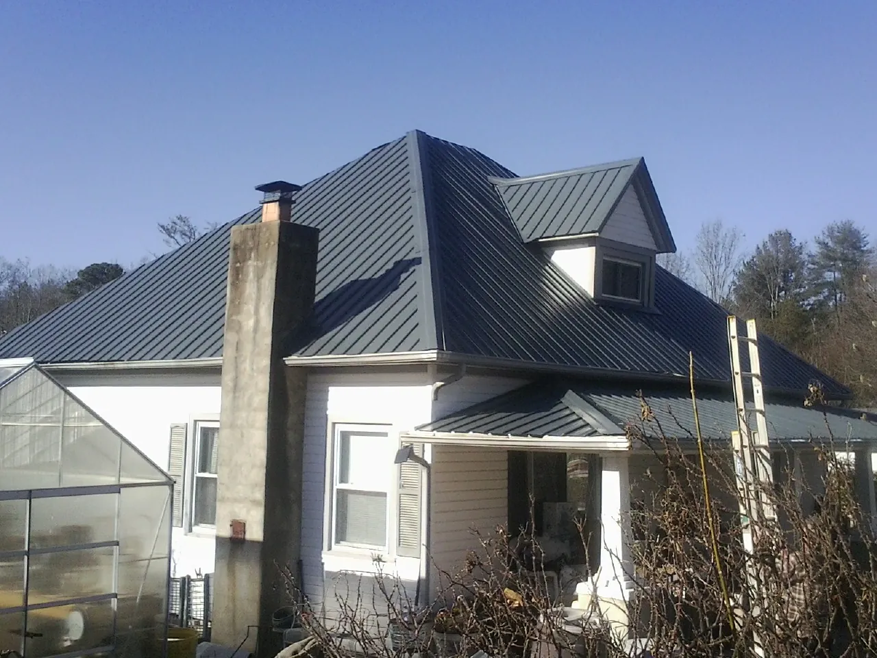 Dark blue standing seam metal roof on a white farmhouse with dormer — Slate & Tile Roof Repair by Roofing Brothers in Mission Hills