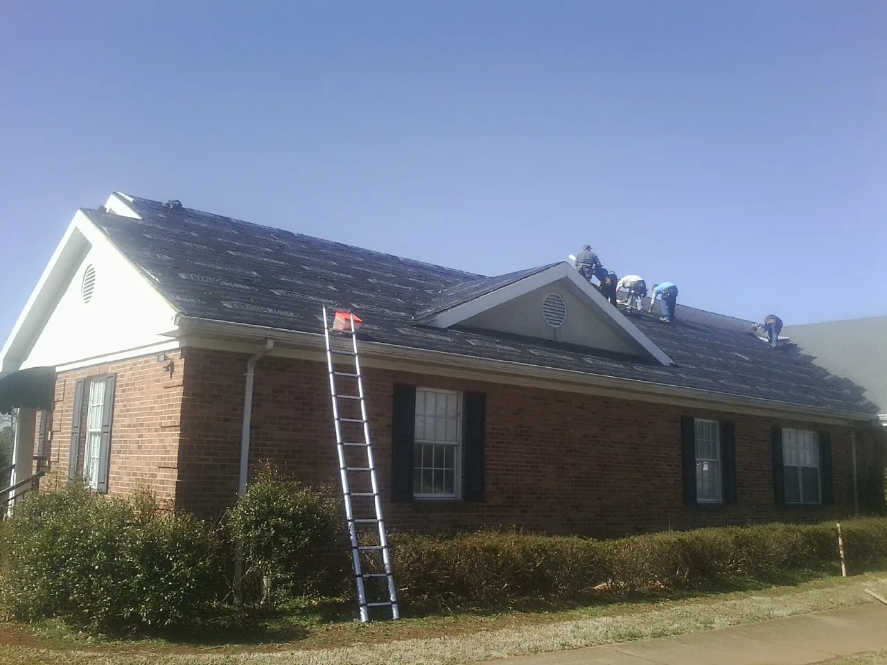 Crew tearing shingles off a brick ranch roof with a ladder set — Metal Roof Repair work by our crew in Mission Hills
