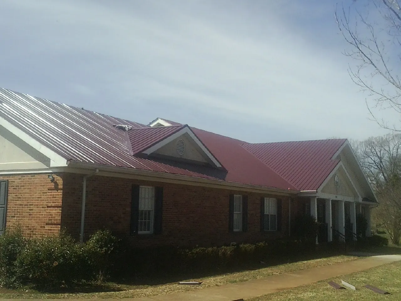 Red metal roof with gabled entries on a long brick building, from a Hail Damage Roof Repair job in Mission Hills