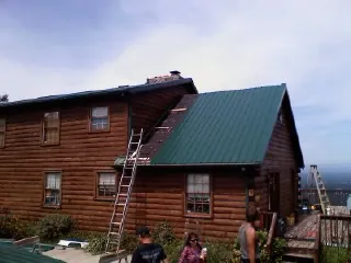 Green metal roof going on a two story log home with ladders set in Mission Hills