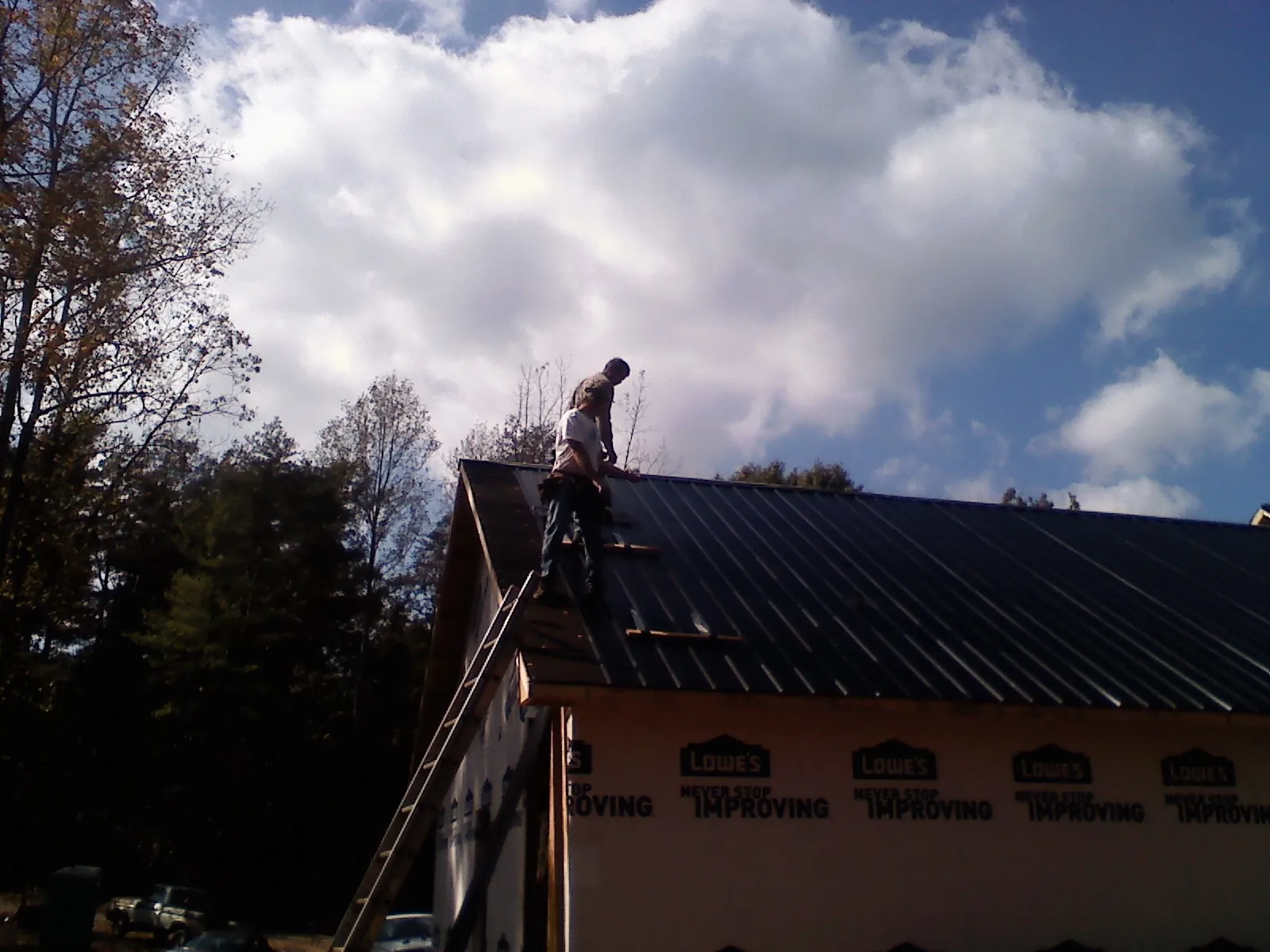Roofer fastening dark metal panels high against a cloudy sky, from a Roof Inspection job in Mission Hills