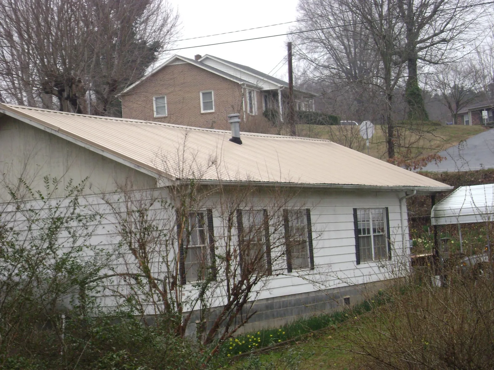 Tan metal roof on a white sided house set into a hillside — Commercial Roofing by Roofing Brothers in Mission Hills